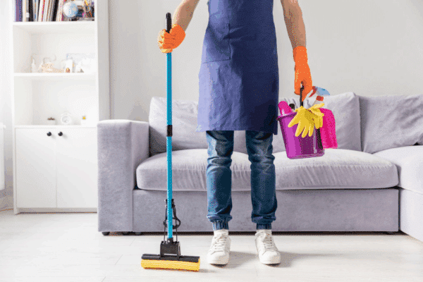 A man in a blue apron holding cleaning supplies, including a mop and bucket