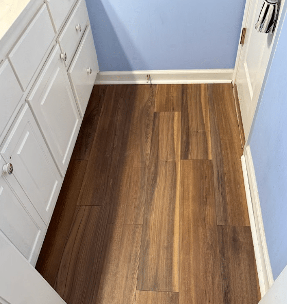 Wood-look hard surface flooring installed in a small residential room beside white cabinets