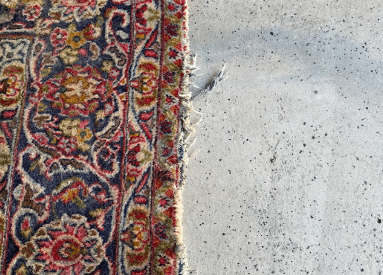 Worn oriental rug edge with frayed fibers resting on concrete floor