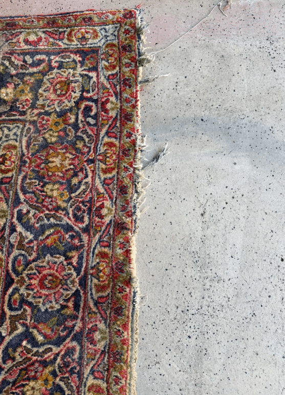 Worn oriental rug edge with frayed fibers resting on concrete floor