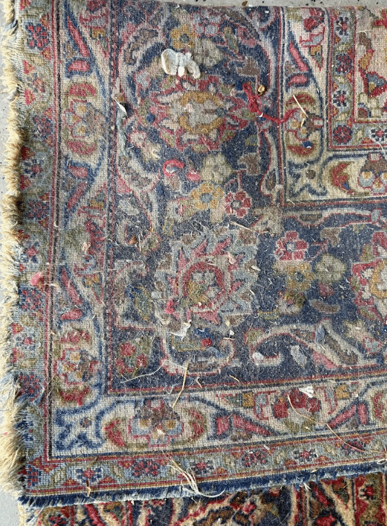 Worn oriental rug with visible tears, loose fibers, and debris trapped in the carpet pile